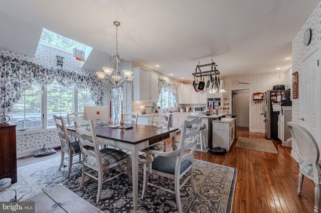 dining room with a notable chandelier, a skylight, wallpapered walls, baseboards, and dark wood-style flooring