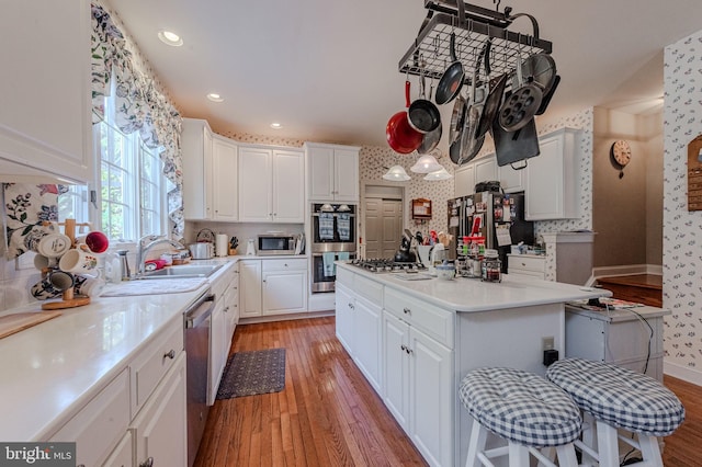 kitchen with white cabinetry, appliances with stainless steel finishes, wallpapered walls, and a sink