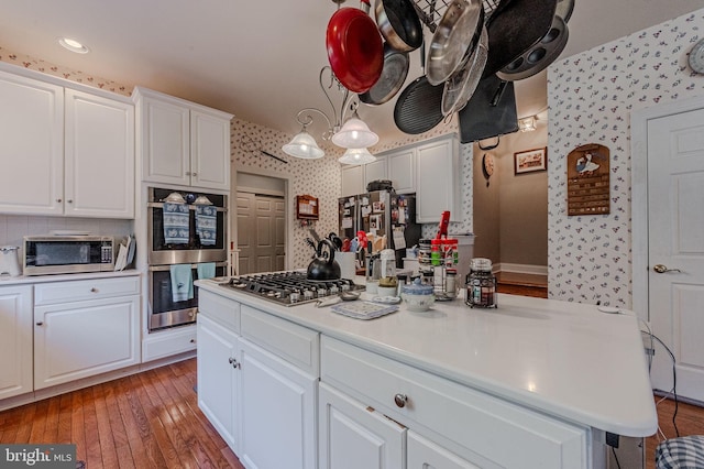 kitchen featuring wallpapered walls, light countertops, white cabinetry, and appliances with stainless steel finishes