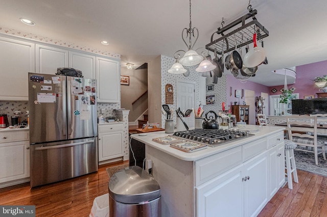 kitchen with white cabinetry, stainless steel appliances, wallpapered walls, and wood finished floors