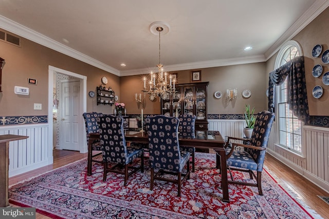 dining room with visible vents, a wainscoted wall, ornamental molding, wood finished floors, and a notable chandelier