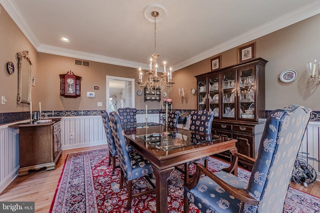 dining room with visible vents, crown molding, a chandelier, a wainscoted wall, and light wood-style floors