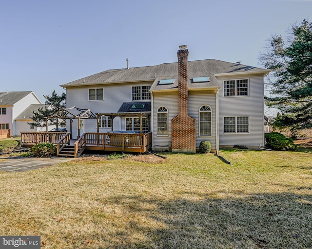 rear view of house with a lawn, roof with shingles, a deck, and a chimney