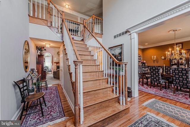 stairs featuring visible vents, crown molding, a chandelier, a towering ceiling, and hardwood / wood-style flooring