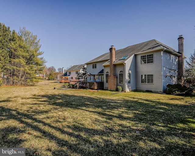 rear view of house with a deck, a lawn, and a chimney