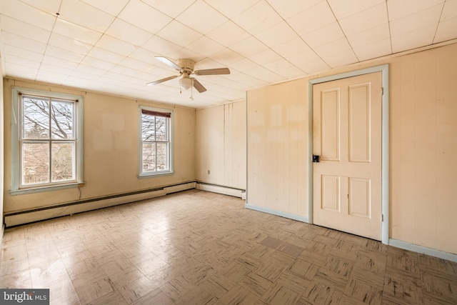 spare room with wooden walls, baseboard heating, baseboards, and a ceiling fan