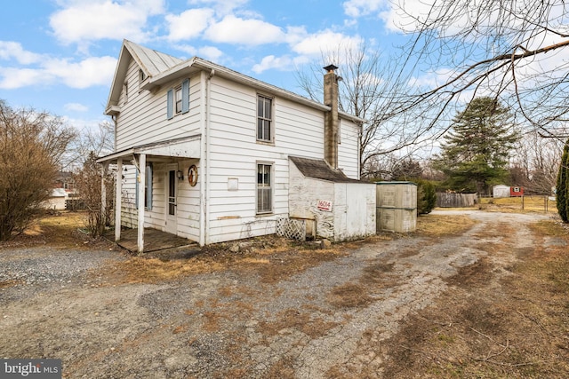 view of side of property with driveway, a chimney, and fence