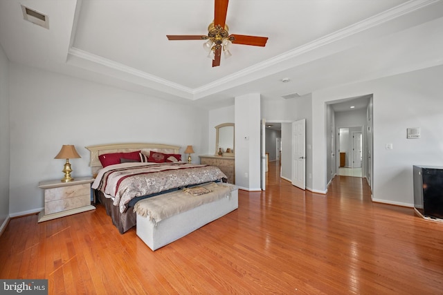 bedroom featuring a raised ceiling, wood finished floors, visible vents, crown molding, and baseboards