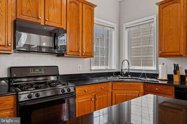 kitchen with brown cabinetry, black appliances, dark stone counters, and a sink