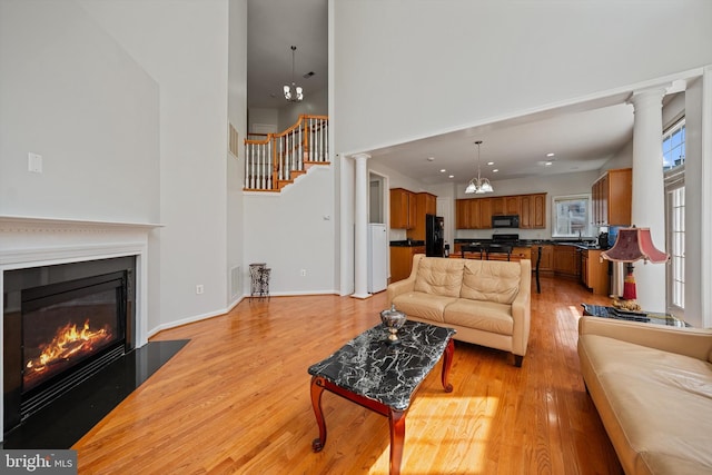 living area with stairs, a fireplace with flush hearth, a towering ceiling, light wood-style flooring, and visible vents