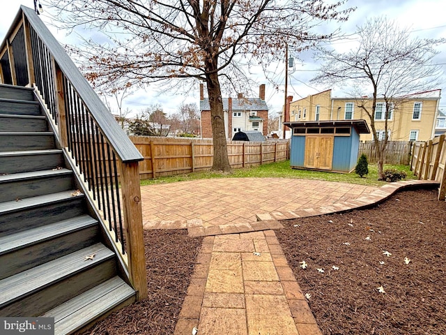 view of yard featuring stairway, a storage shed, a fenced backyard, an outdoor structure, and a patio area