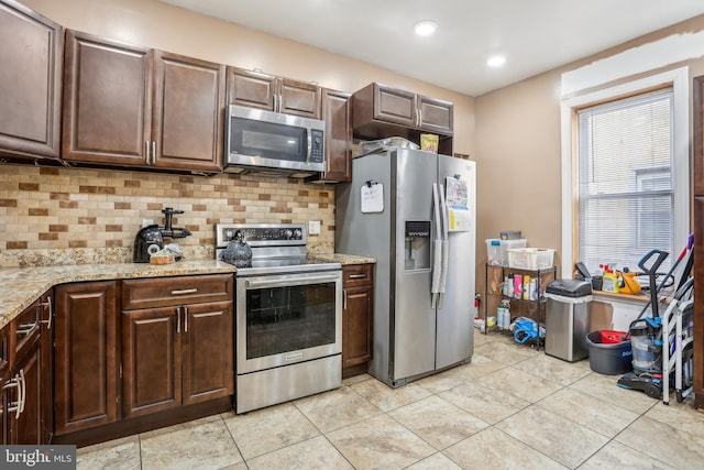 kitchen with tasteful backsplash, appliances with stainless steel finishes, light stone counters, and light tile patterned flooring