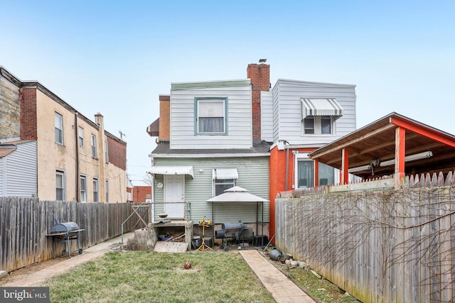 rear view of house with a chimney, a yard, and fence