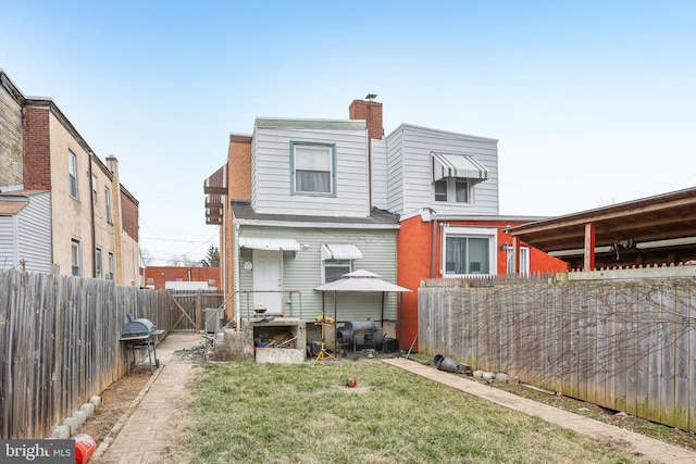 back of house featuring a yard, a fenced backyard, and a chimney