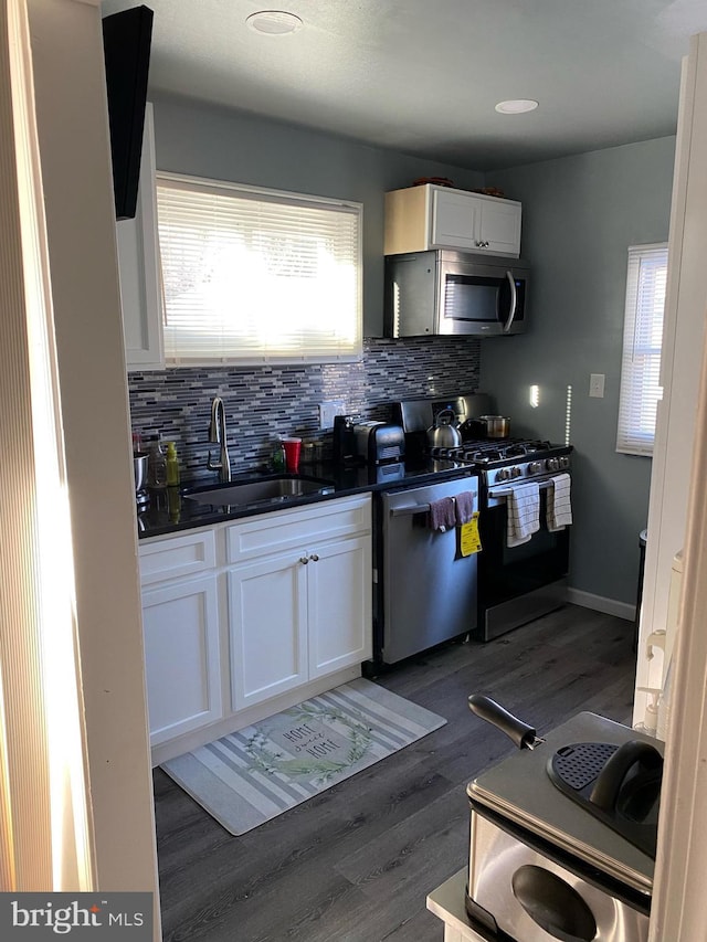 kitchen with wood finished floors, a sink, appliances with stainless steel finishes, dark countertops, and tasteful backsplash