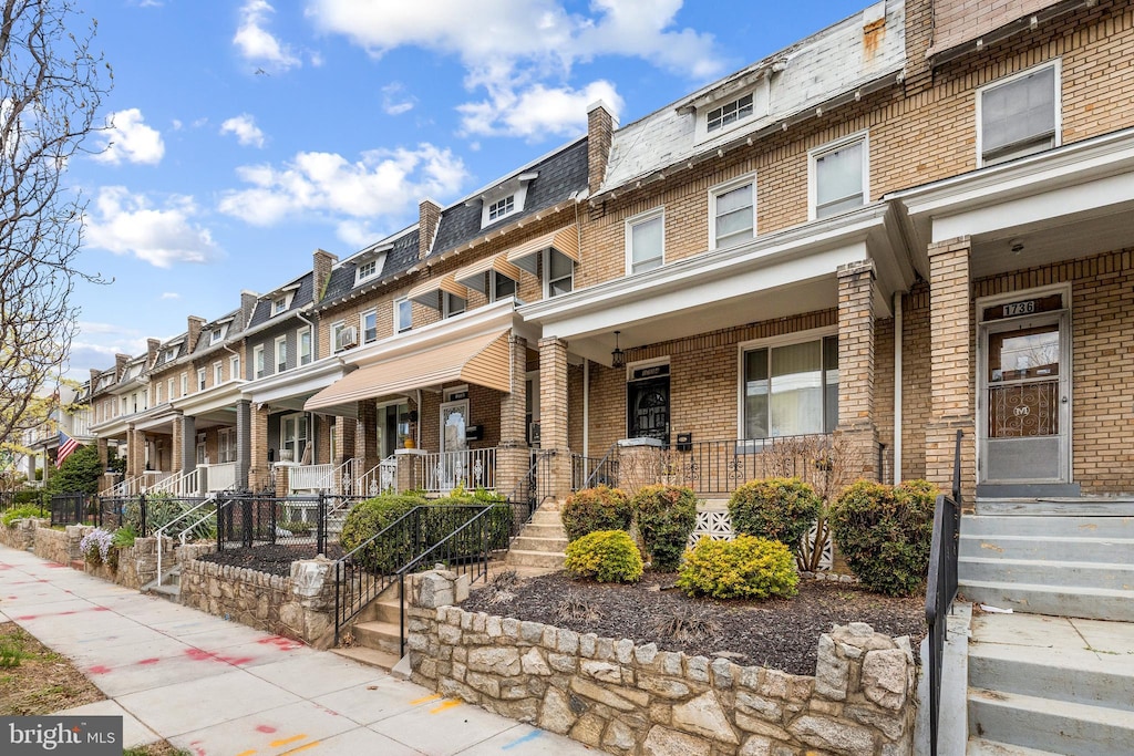 multi unit property featuring brick siding, a porch, a residential view, and mansard roof