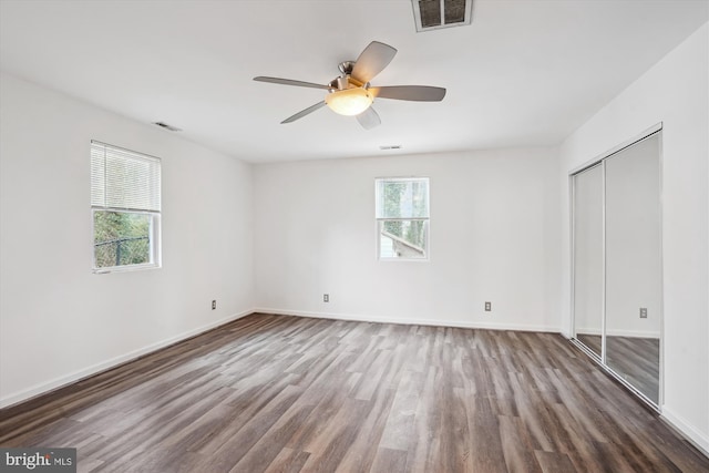 unfurnished bedroom featuring wood finished floors, visible vents, baseboards, ceiling fan, and a closet