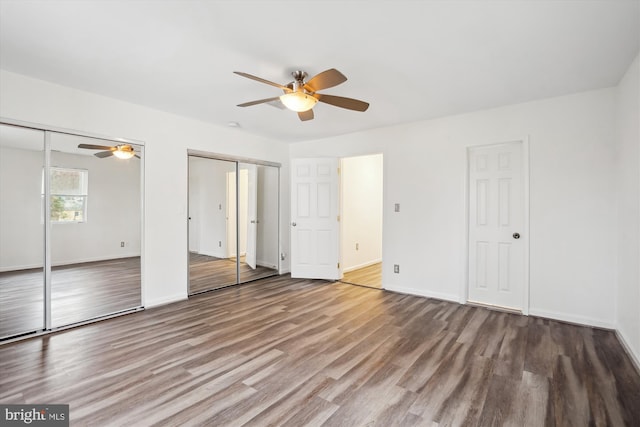 unfurnished bedroom featuring wood finished floors, baseboards, and two closets