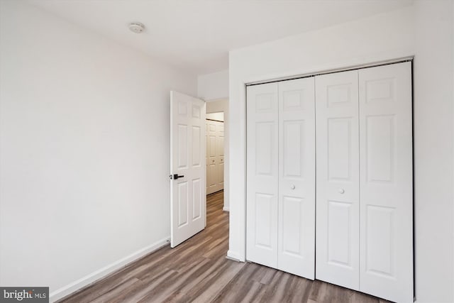 unfurnished bedroom featuring wood finished floors, baseboards, and a closet