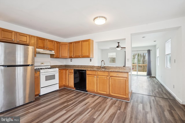 kitchen with white gas stove, under cabinet range hood, black dishwasher, freestanding refrigerator, and a sink