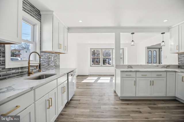 kitchen with light stone counters, a sink, white cabinets, light wood-style floors, and dishwasher