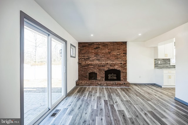 unfurnished living room with light wood finished floors, visible vents, a fireplace, and baseboards