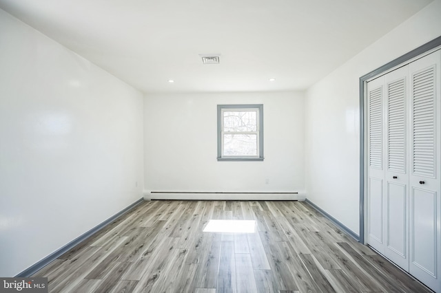 unfurnished bedroom with a closet, wood finished floors, visible vents, and baseboard heating