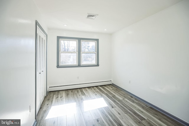 unfurnished bedroom with a closet, baseboard heating, visible vents, and wood finished floors