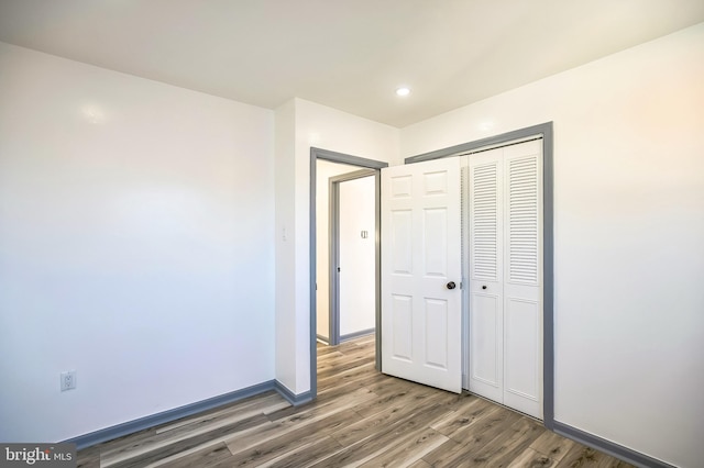 unfurnished bedroom featuring recessed lighting, a closet, baseboards, and wood finished floors