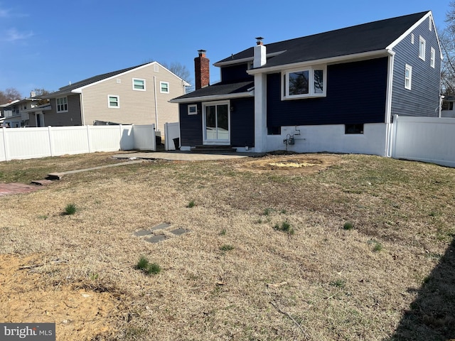 rear view of house with a yard, entry steps, a chimney, and fence