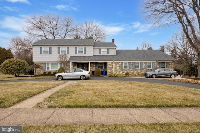 view of front of house featuring a front yard, stone siding, roof with shingles, and a chimney