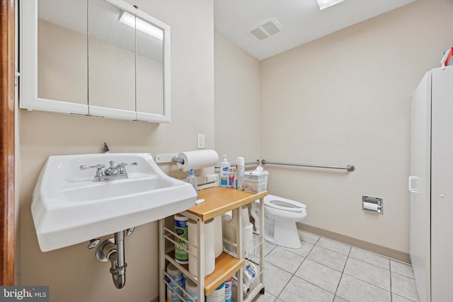 half bathroom featuring visible vents, baseboards, toilet, tile patterned floors, and a sink