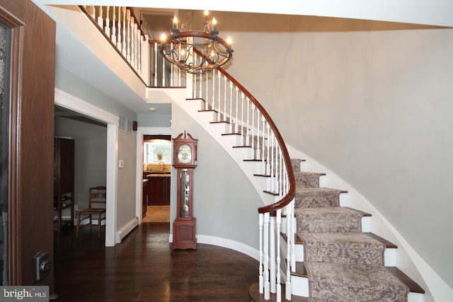 stairs featuring a chandelier, a high ceiling, baseboards, and wood finished floors