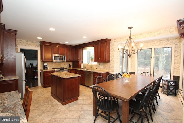 kitchen with a sink, a center island, stainless steel appliances, wallpapered walls, and a chandelier