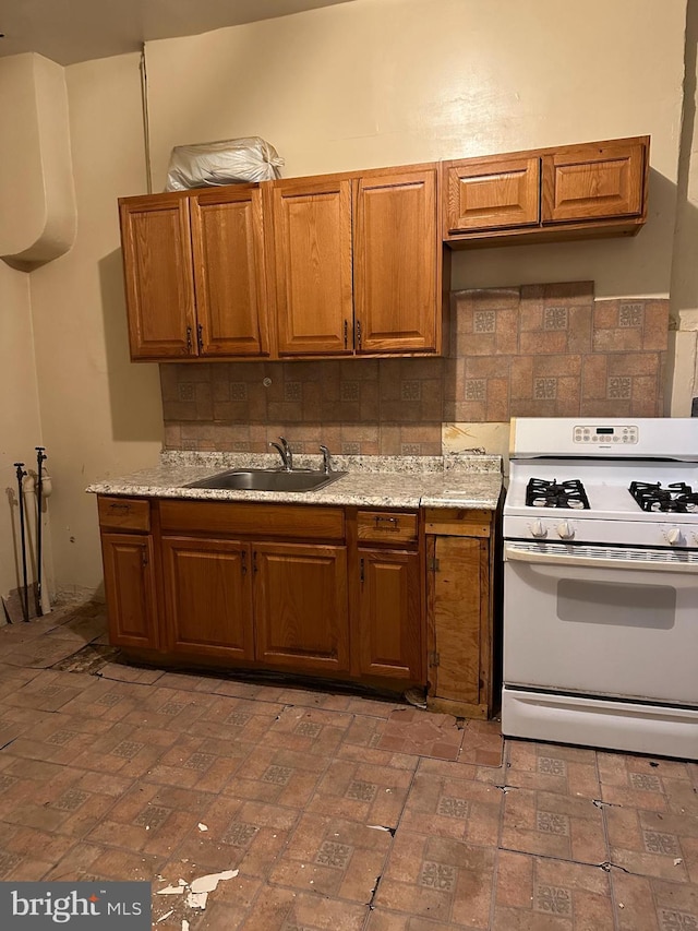 kitchen with brown cabinets, white range with gas cooktop, brick floor, a sink, and tasteful backsplash