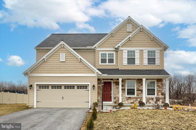 view of front of home featuring fence, roof with shingles, covered porch, stone siding, and driveway