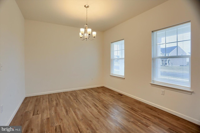 unfurnished room with an inviting chandelier, wood finished floors, baseboards, and visible vents