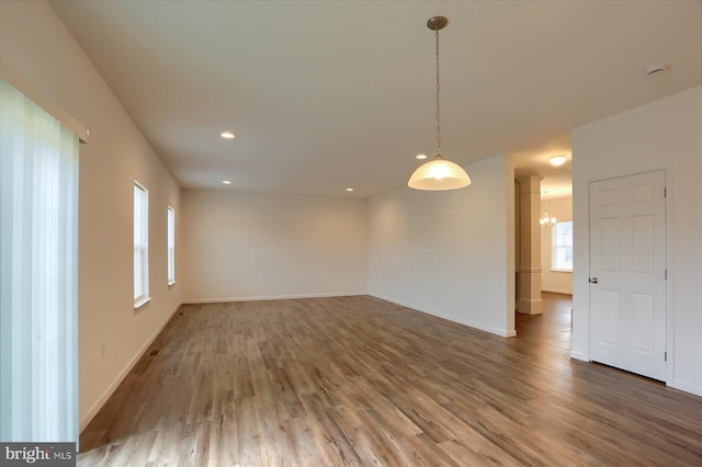 empty room with a notable chandelier, recessed lighting, baseboards, and wood finished floors