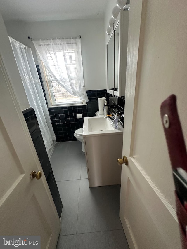 bathroom featuring tile patterned floors, toilet, tile walls, wainscoting, and vanity