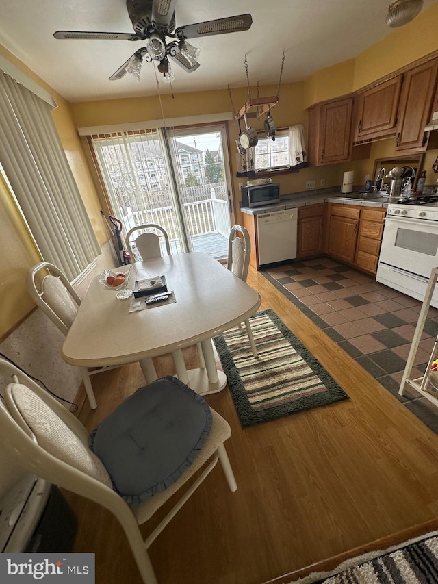 kitchen with ceiling fan, dark wood finished floors, brown cabinetry, white appliances, and a sink