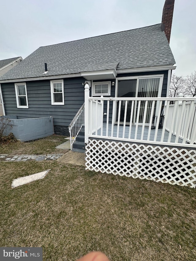 back of house featuring a wooden deck, a lawn, a chimney, and roof with shingles