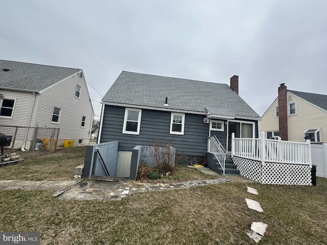 back of house with a deck, fence, a yard, roof with shingles, and a chimney