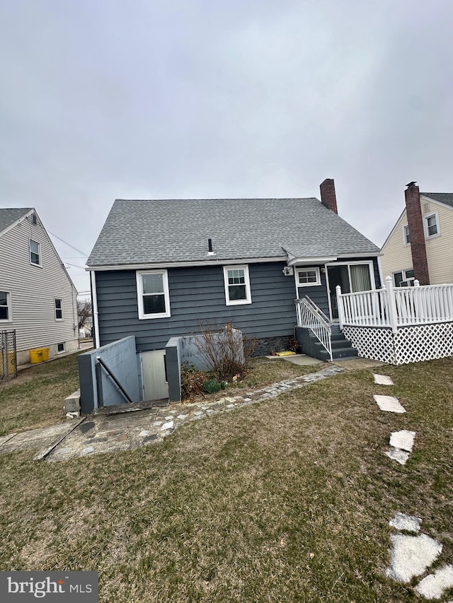 rear view of house with a chimney, a wooden deck, a shingled roof, and a yard