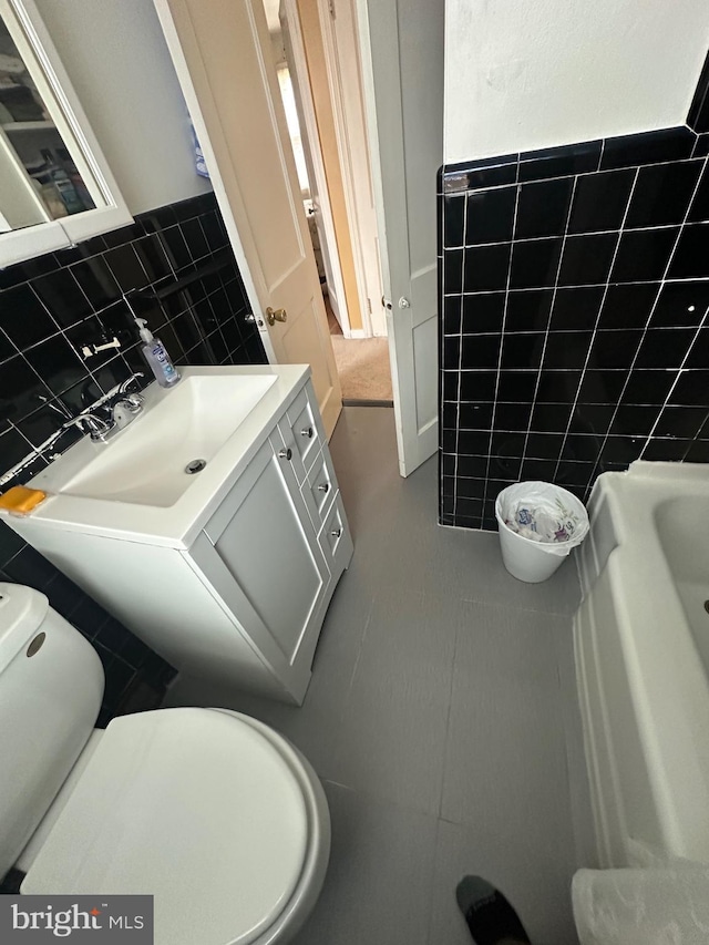 bathroom featuring toilet, vanity, a bathing tub, tile patterned floors, and tile walls