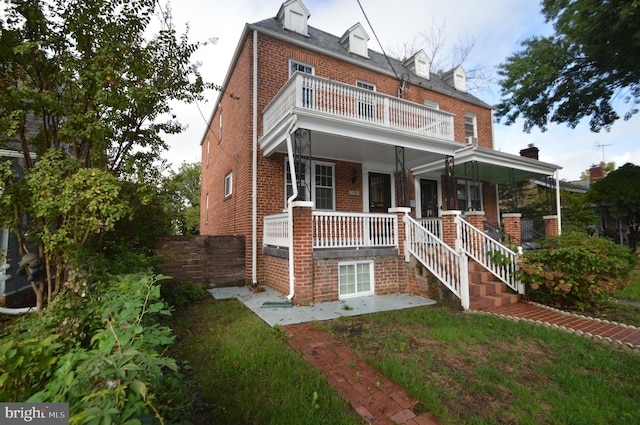 view of front of home featuring a balcony, fence, covered porch, a front yard, and brick siding