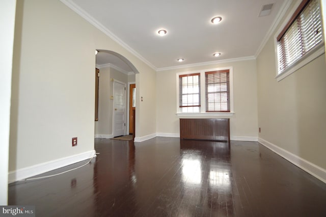 spare room featuring baseboards, visible vents, arched walkways, dark wood-style flooring, and crown molding