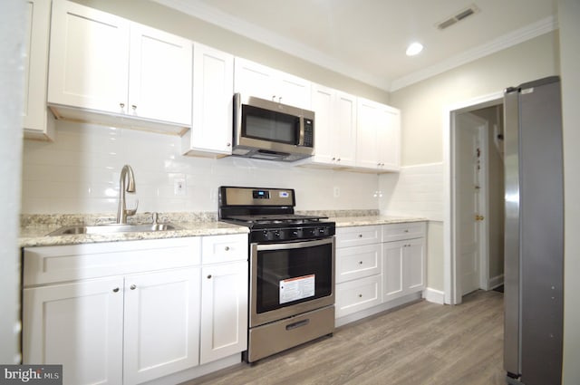 kitchen with ornamental molding, light wood-style flooring, appliances with stainless steel finishes, white cabinetry, and a sink