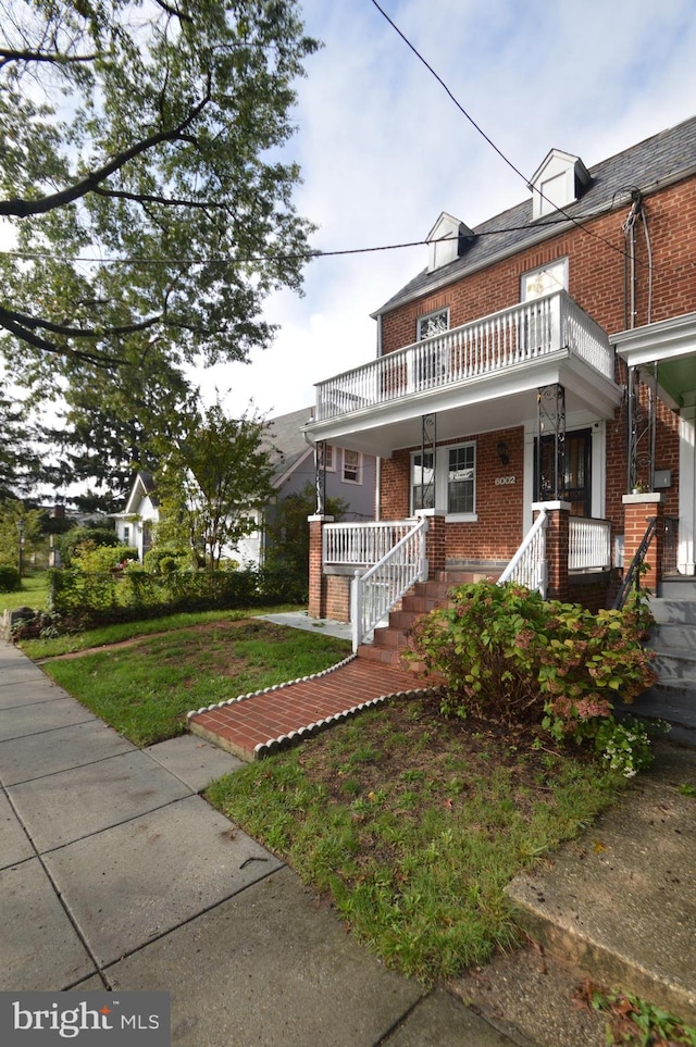 view of front of property featuring brick siding, a porch, a front yard, and a balcony