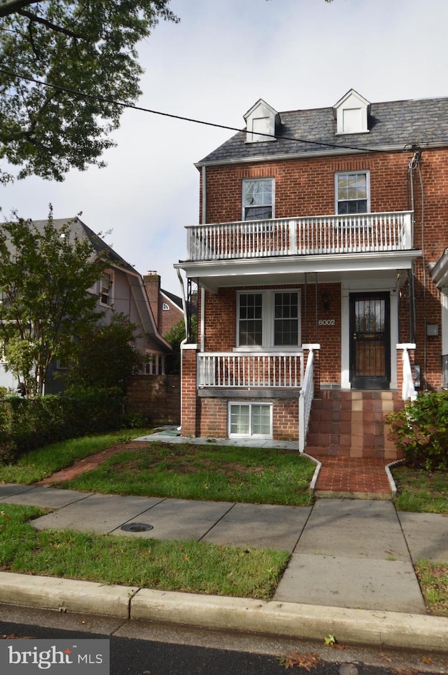 view of front of home with a front lawn, brick siding, covered porch, and a balcony