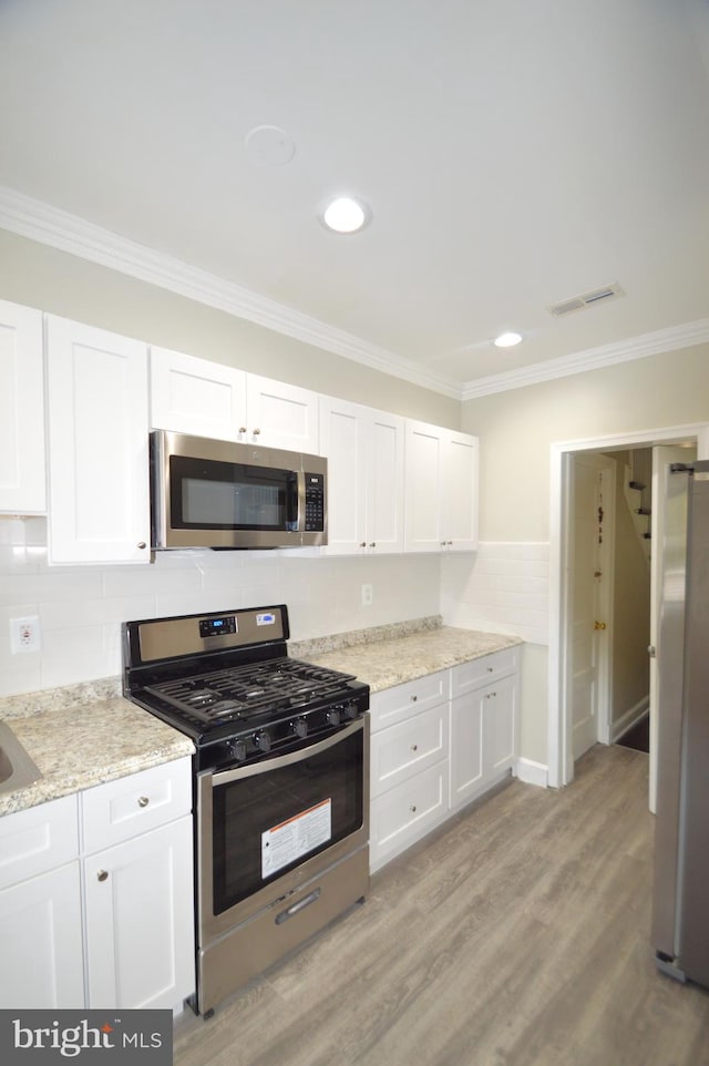 kitchen featuring visible vents, crown molding, stainless steel appliances, and light wood-type flooring